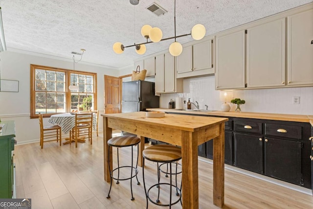 kitchen with dark cabinets, a sink, light wood-style floors, hanging light fixtures, and freestanding refrigerator