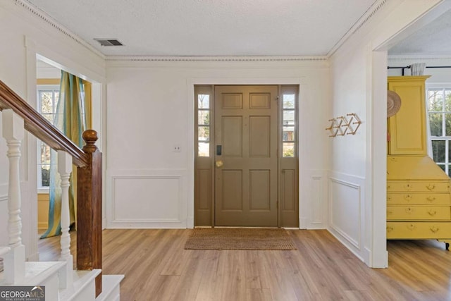 entrance foyer with crown molding, visible vents, a textured ceiling, light wood-type flooring, and stairs