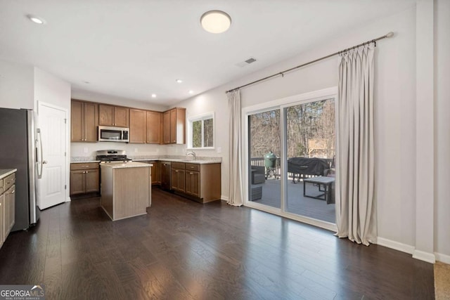 kitchen with stainless steel appliances, dark wood-type flooring, a kitchen island, light countertops, and brown cabinets