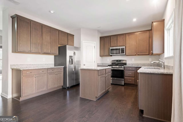 kitchen with appliances with stainless steel finishes, dark wood finished floors, light stone counters, and a center island