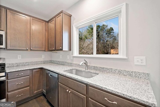 kitchen with appliances with stainless steel finishes, dark wood-type flooring, a sink, and light stone counters