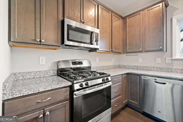 kitchen with stainless steel appliances, dark wood-style flooring, and light stone countertops