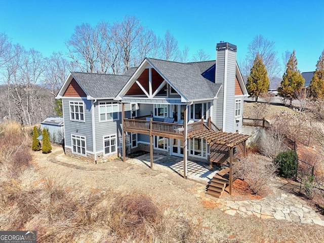 back of house featuring roof with shingles, a chimney, a patio area, a deck, and driveway