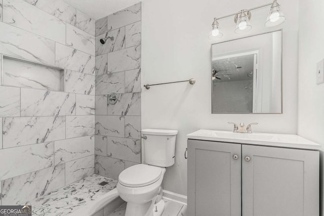 bathroom with marble finish floor, tiled shower, vanity, and toilet