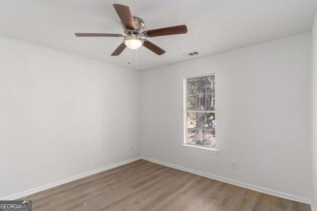 empty room featuring light wood finished floors, a ceiling fan, visible vents, and baseboards