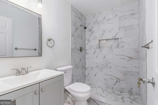 bathroom featuring marble finish floor, a tile shower, vanity, and toilet