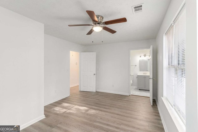 unfurnished bedroom featuring baseboards, visible vents, ensuite bath, wood finished floors, and a textured ceiling