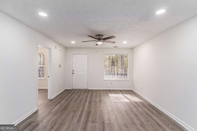 unfurnished room with a textured ceiling, recessed lighting, wood finished floors, and baseboards