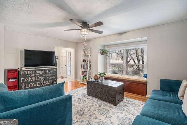 living room with ceiling fan, a textured ceiling, baseboards, and wood finished floors