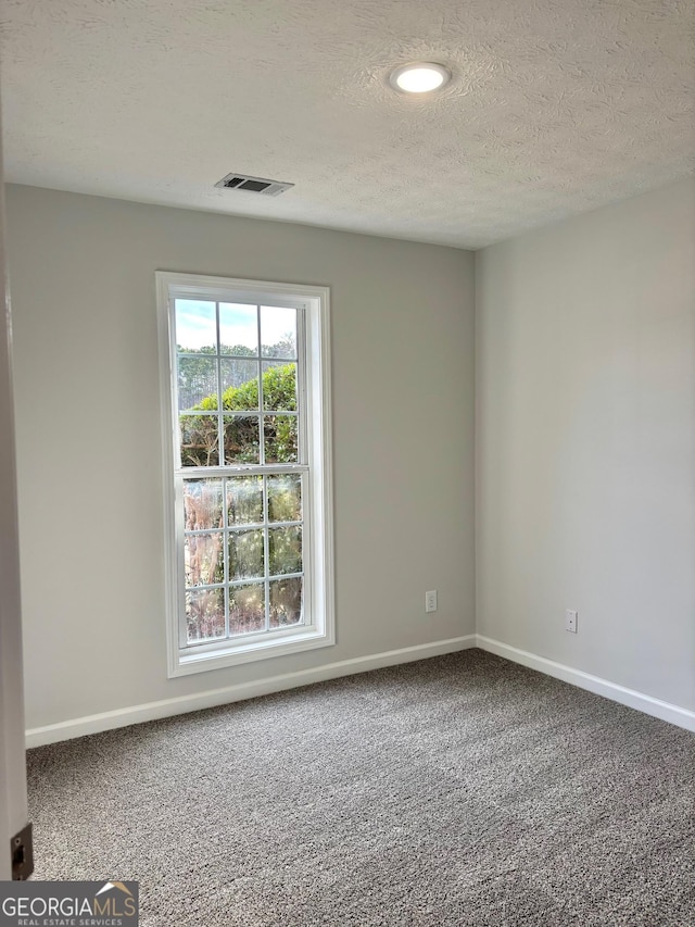 carpeted empty room featuring a textured ceiling, visible vents, and baseboards