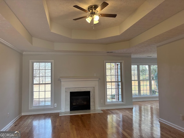 unfurnished living room with a textured ceiling, a tray ceiling, plenty of natural light, and wood finished floors