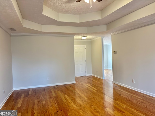 unfurnished room with a textured ceiling, ceiling fan, wood finished floors, baseboards, and a tray ceiling