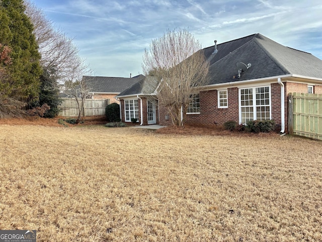 rear view of property with brick siding, a lawn, a shingled roof, and fence