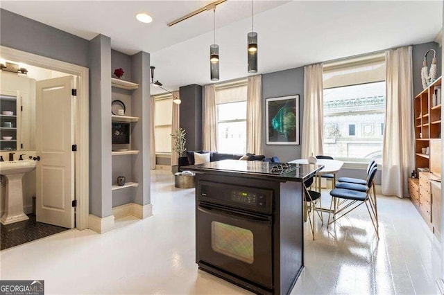 kitchen with a sink, black oven, built in shelves, and hanging light fixtures