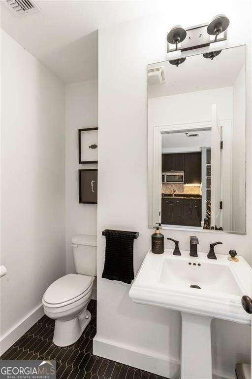 half bath featuring toilet, a sink, visible vents, and baseboards