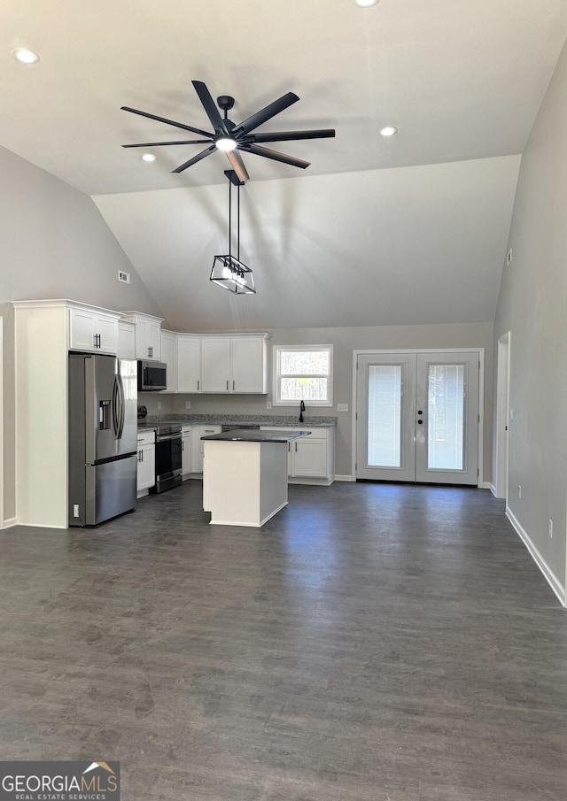 kitchen with stainless steel appliances, dark countertops, open floor plan, white cabinets, and vaulted ceiling