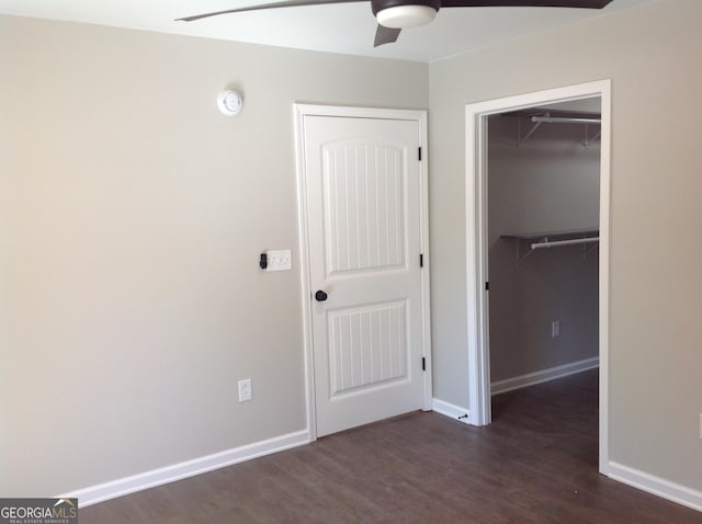 unfurnished bedroom with a closet, baseboards, a walk in closet, and dark wood-type flooring