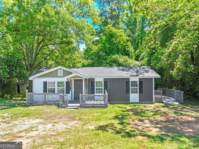 view of front of home with a front yard, roof with shingles, and a wooden deck