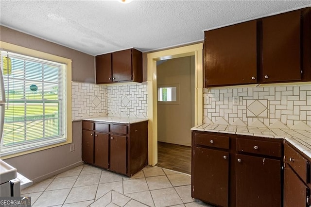 kitchen with light tile patterned floors, light countertops, backsplash, a textured ceiling, and dark brown cabinets