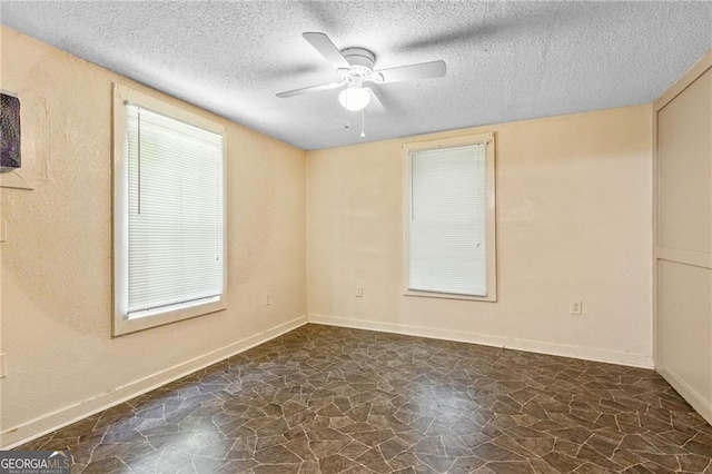 empty room featuring stone flooring, a textured wall, a ceiling fan, a textured ceiling, and baseboards