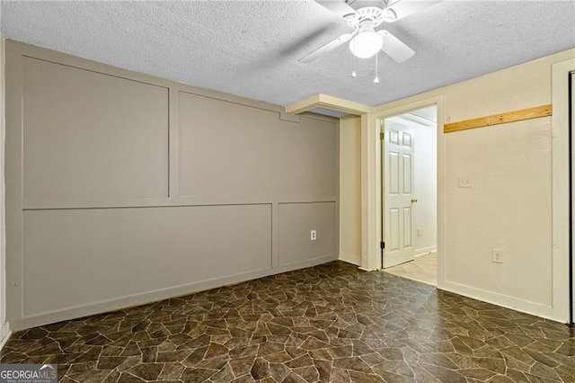 unfurnished bedroom featuring a ceiling fan, stone finish flooring, a decorative wall, and a textured ceiling