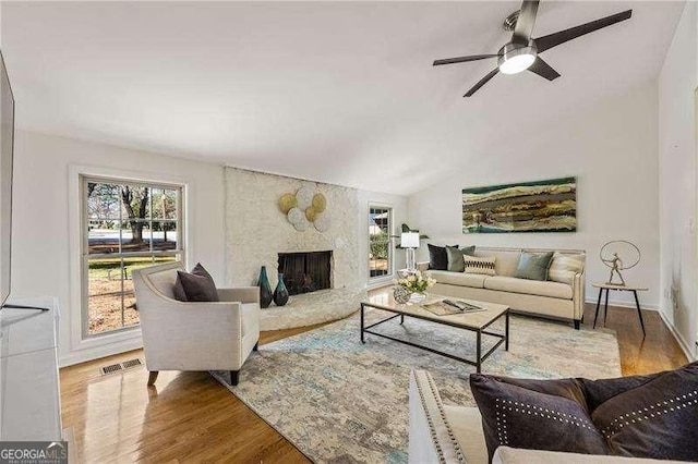 living area with lofted ceiling, a fireplace, wood finished floors, visible vents, and baseboards