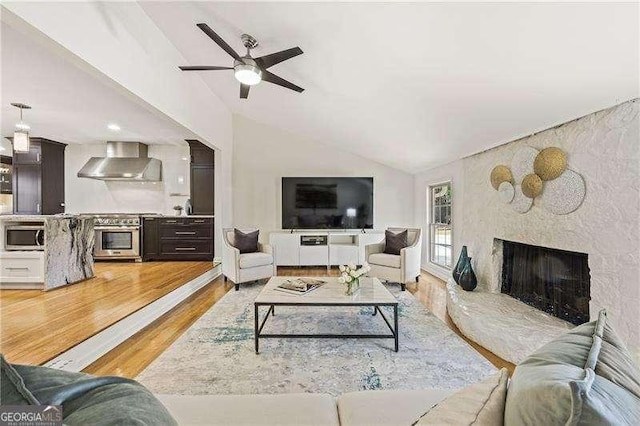 living area with lofted ceiling, a fireplace, a ceiling fan, and light wood-style floors