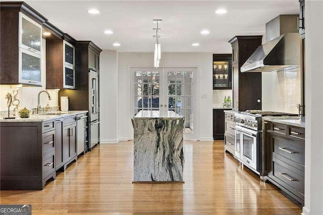 kitchen featuring light stone counters, a center island, french doors, high end appliances, and light wood-type flooring