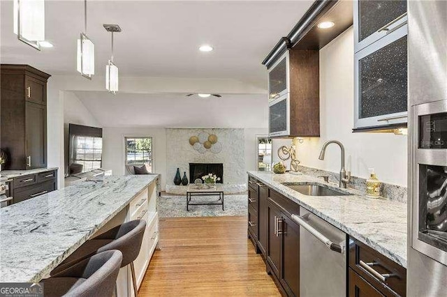 kitchen with light wood-style flooring, a fireplace, a sink, dark brown cabinets, and dishwasher