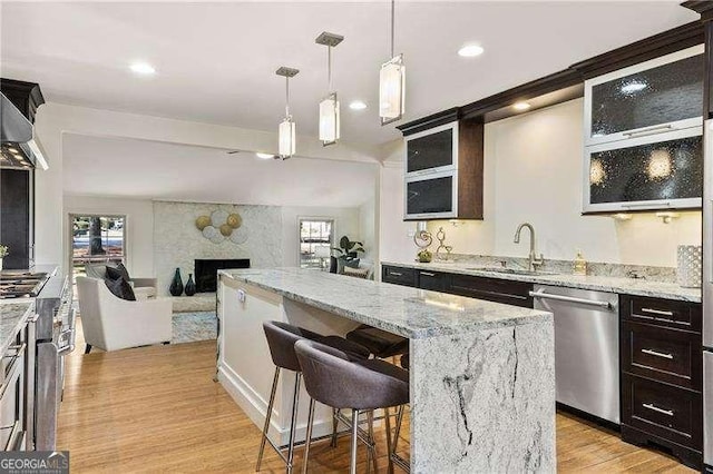 kitchen featuring a large fireplace, a kitchen island, stainless steel appliances, light wood-style floors, and a sink