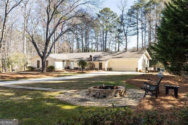 ranch-style home with a garage, concrete driveway, and a fire pit