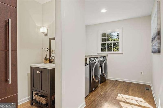 clothes washing area with washer and clothes dryer, wood finished floors, and baseboards