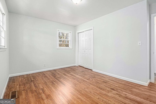 unfurnished bedroom featuring baseboards, visible vents, a closet, and wood finished floors