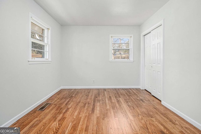 unfurnished bedroom featuring a closet, visible vents, baseboards, and wood finished floors