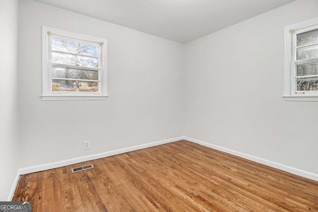 unfurnished room featuring visible vents, plenty of natural light, baseboards, and wood finished floors