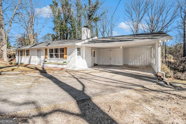 view of front of house with an attached carport, brick siding, driveway, and a chimney