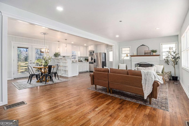 living room featuring baseboards, visible vents, wood finished floors, french doors, and a brick fireplace