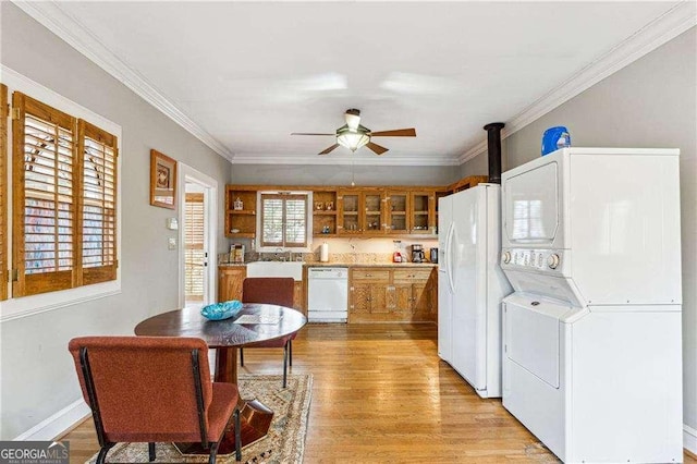 kitchen featuring brown cabinets, light wood-style flooring, stacked washing maching and dryer, white appliances, and crown molding