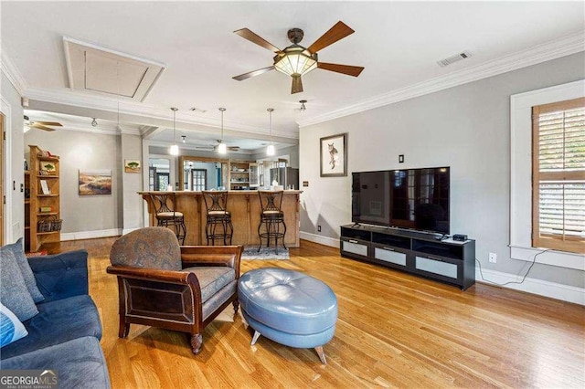 living area featuring visible vents, light wood-style flooring, attic access, and crown molding