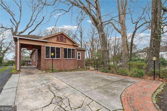 view of property exterior with an attached carport, brick siding, driveway, and fence