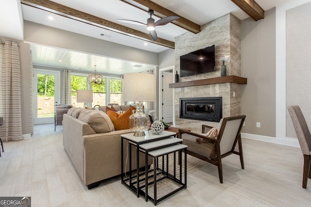 living room featuring light wood-type flooring, a tile fireplace, beamed ceiling, and baseboards