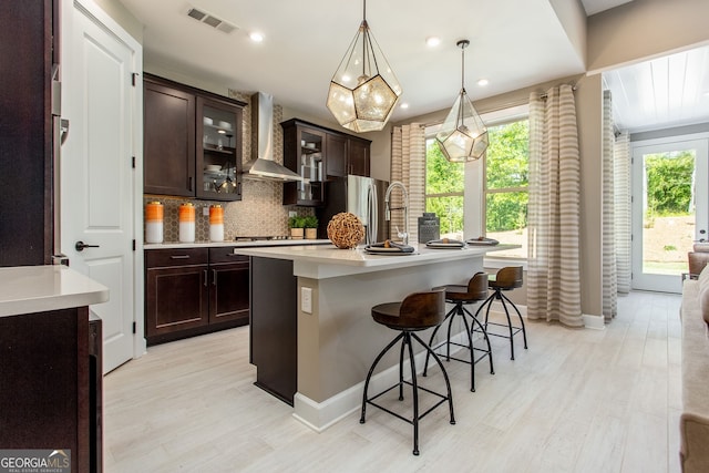 kitchen with tasteful backsplash, visible vents, freestanding refrigerator, light countertops, and wall chimney range hood