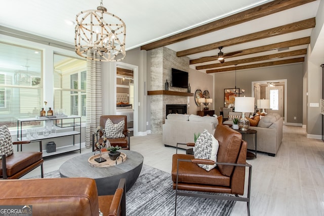 living room with ceiling fan with notable chandelier, beamed ceiling, a fireplace, and a healthy amount of sunlight