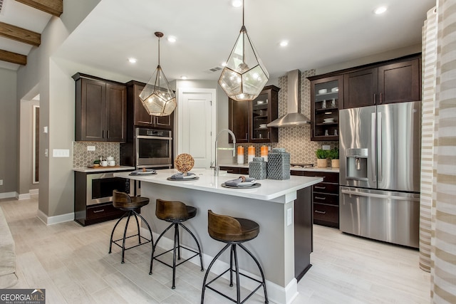 kitchen with stainless steel appliances, light countertops, wall chimney range hood, and dark brown cabinets