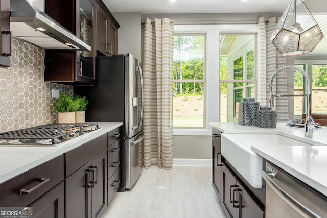 kitchen with dark brown cabinetry, wall chimney range hood, stainless steel appliances, and light countertops