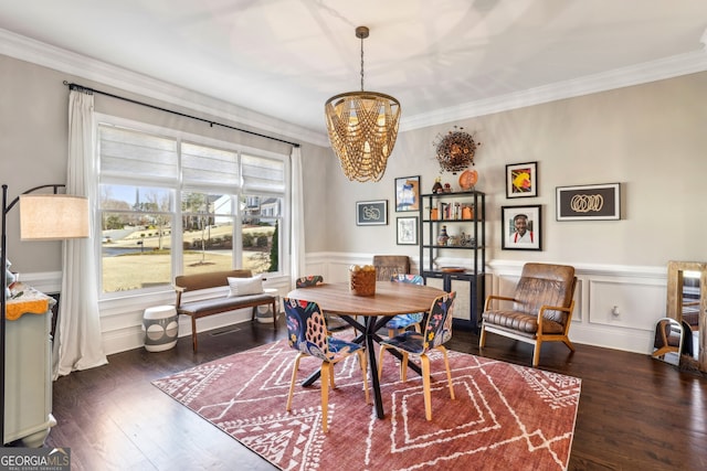 dining area with a wainscoted wall, ornamental molding, dark wood-style flooring, and an inviting chandelier