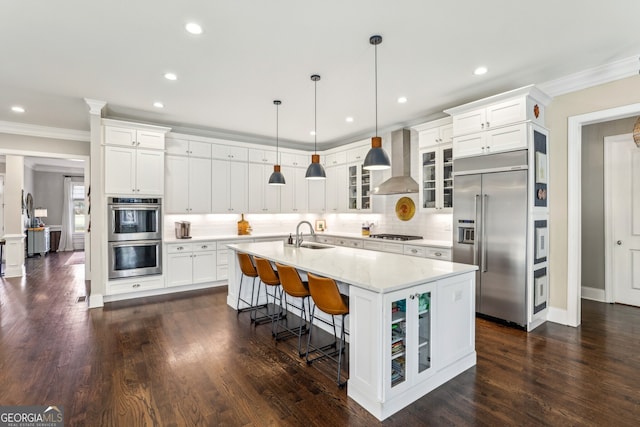 kitchen featuring wall chimney exhaust hood, glass insert cabinets, appliances with stainless steel finishes, ornamental molding, and a sink