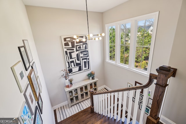 staircase with a notable chandelier, wood finished floors, and baseboards