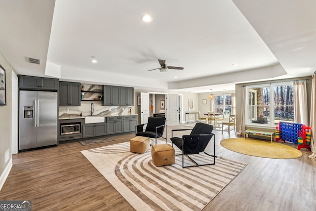 living area featuring a tray ceiling, recessed lighting, visible vents, a ceiling fan, and wood finished floors