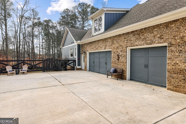 view of side of property featuring driveway, brick siding, board and batten siding, and a shingled roof